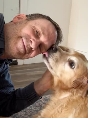 Jeff Lydon leaning towards his dog Holly who is licking his face.