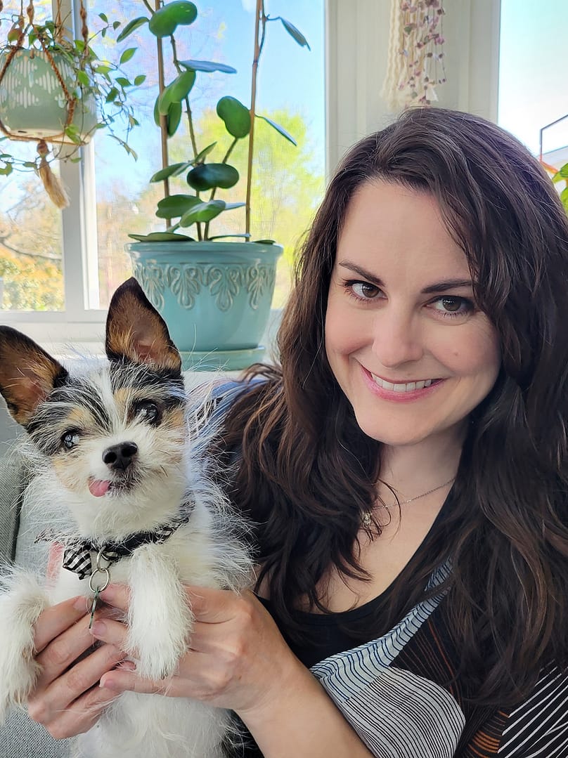 Holley Hayes holding her small senior dog who has its tongue sticking out.